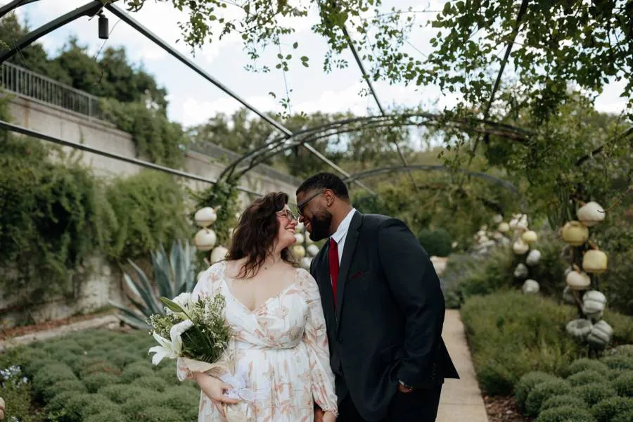 Hailey and Tristan laughing nose-to-nose beneath an iron garden arch