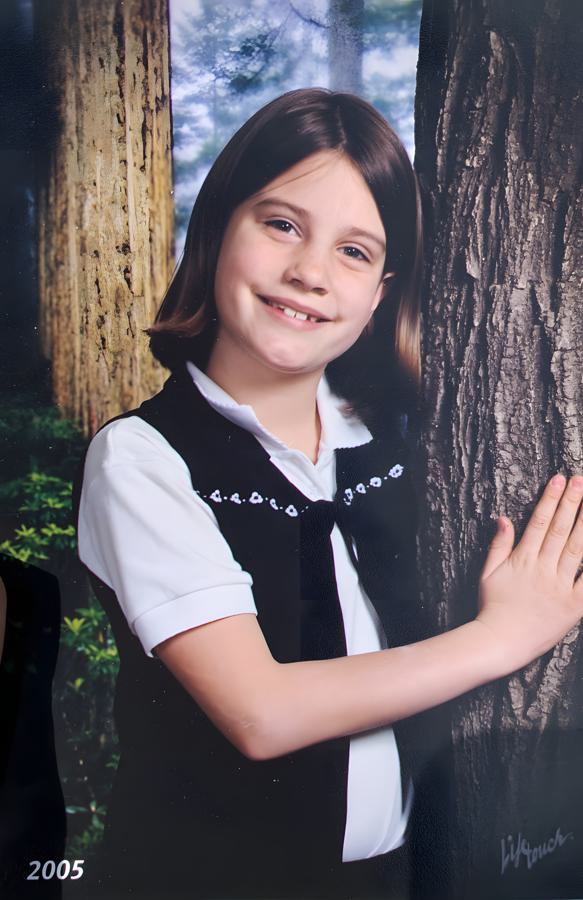 Hailey's 2005 school portrait, smiling beside a painted forest backdrop